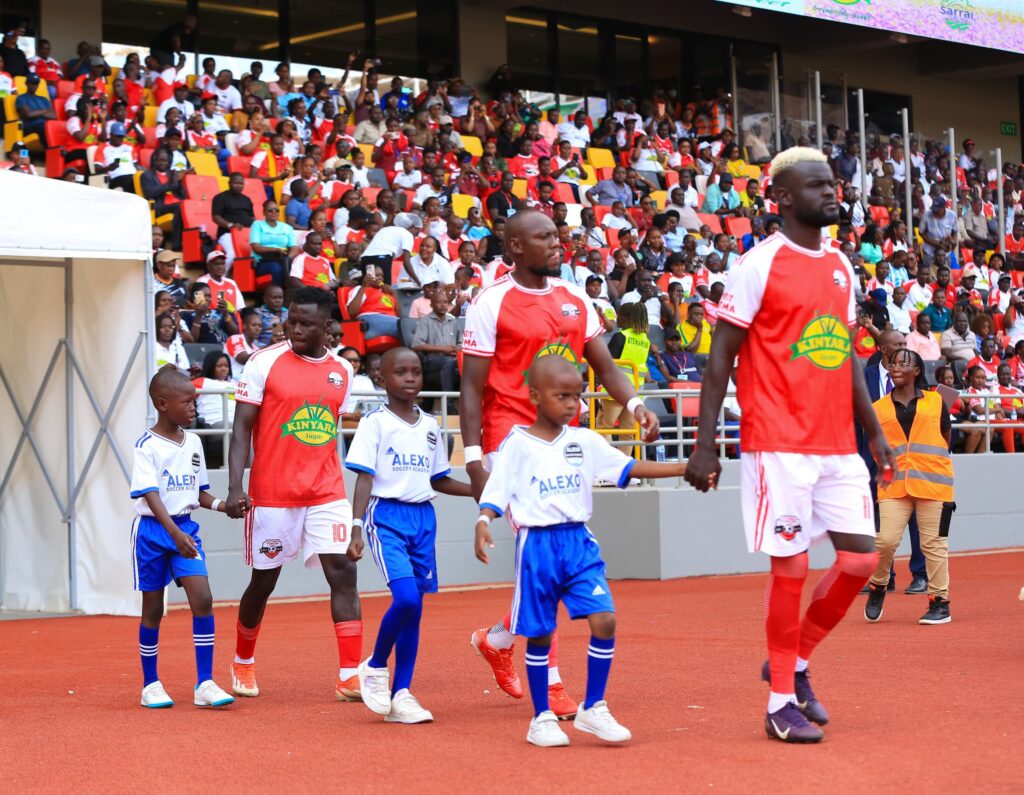 Kitara FC players walk onto the pitch with young mascots before a match at Hoima City Stadium.