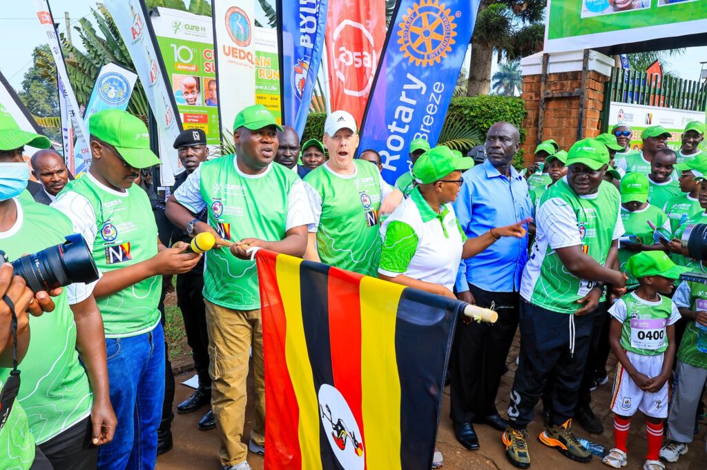 Speaker Jacob Marksons Oboth holds the Ugandan flag alongside participants at the 10th CURE Brain Surgery Run in Mbale.