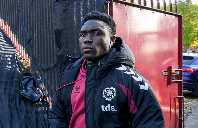 Rogers Mato wearing a black Hearts jacket over a maroon training top and carrying a wash bag.