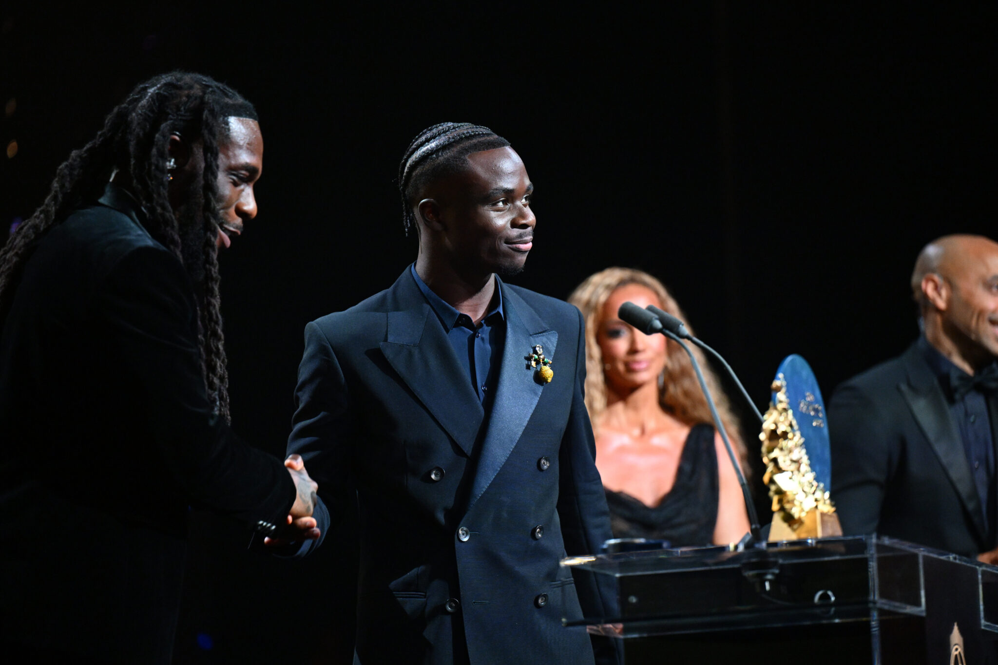Bukayo Saka shakes hands with Burna Boy beside the Sócrates Award trophy at the 2026 Ballon d’Or ceremony.